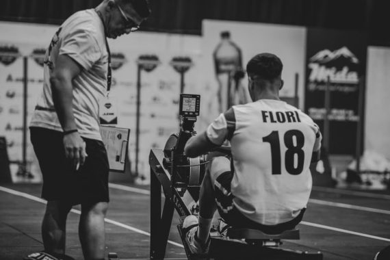 An athlete using a rowing machine indoors, coached in a gym setting.